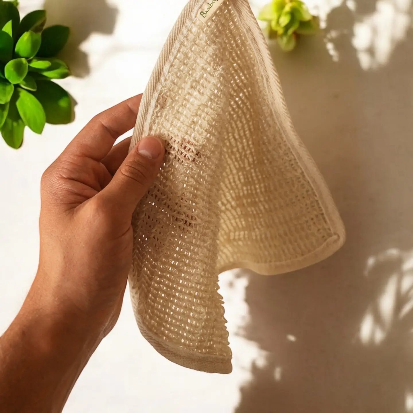 Hand holding a beige textured towel with plants in the background