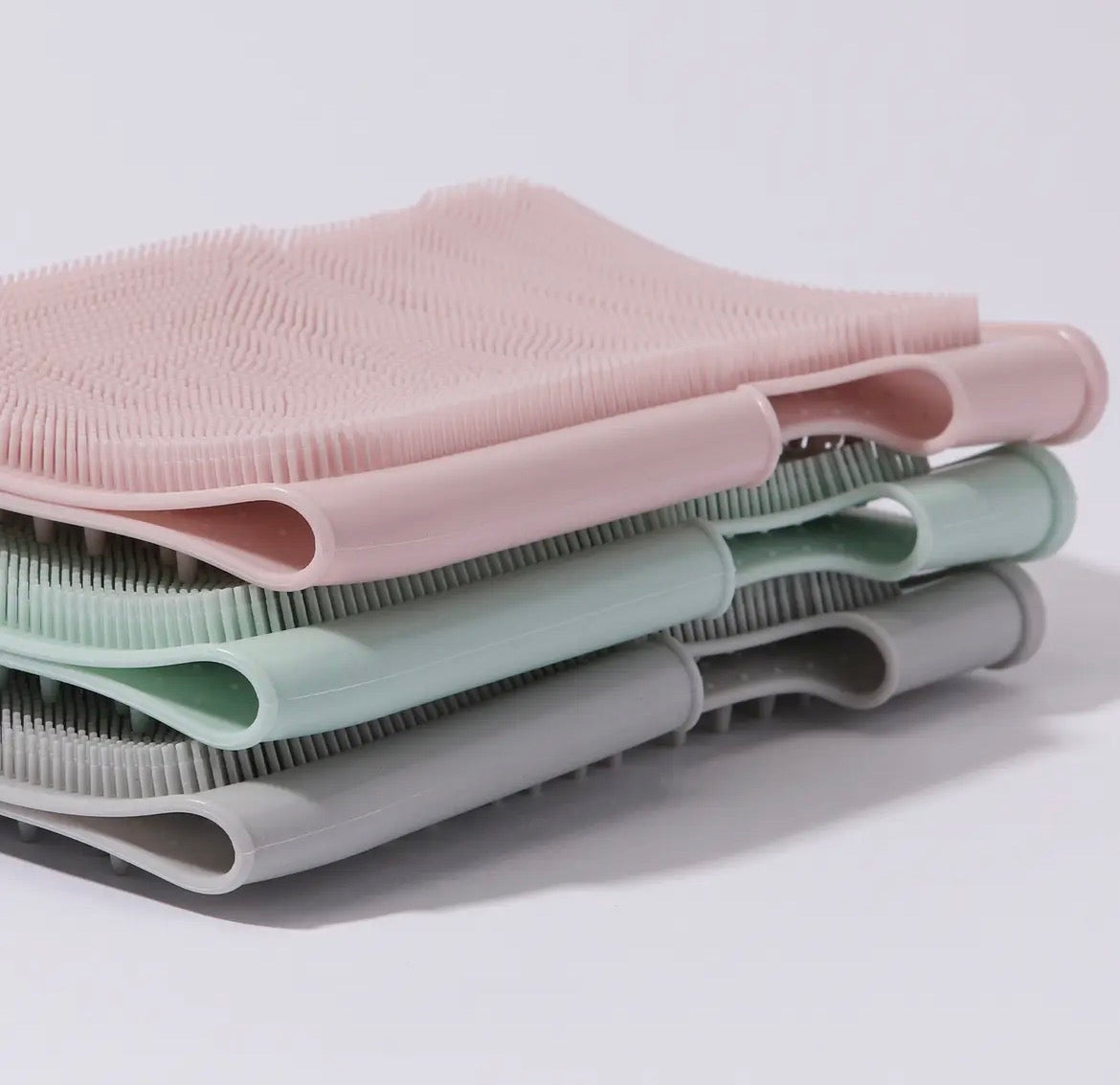 Stack of pink, green, and gray silicone scrubbers on a white background