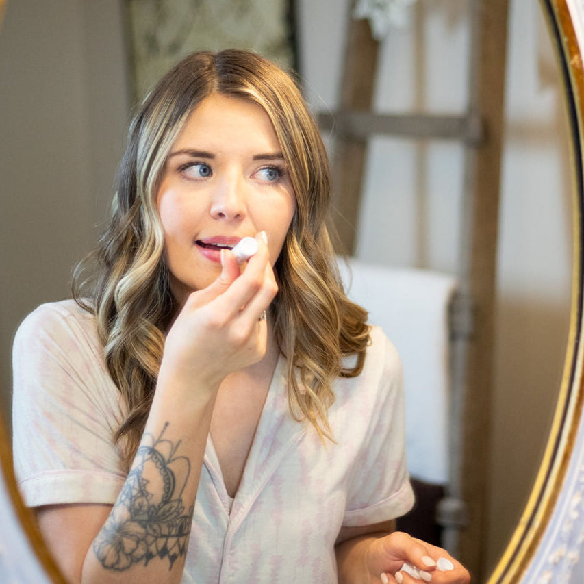 woman applying scrub me good lip balm while looking in a mirror