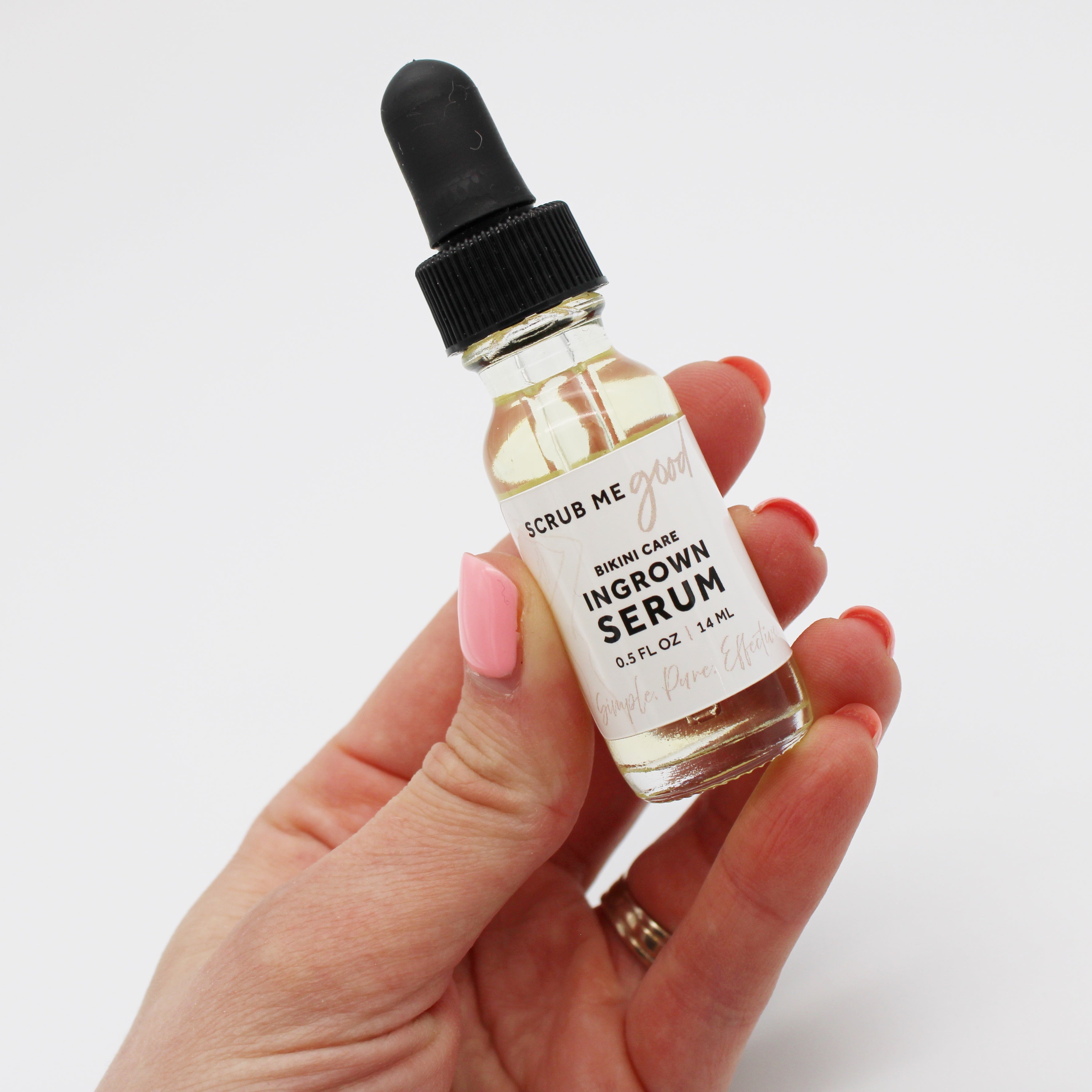 Hand holding a small bottle of 'Scrub Me Good' ingrown serum with a dropper on a white background.