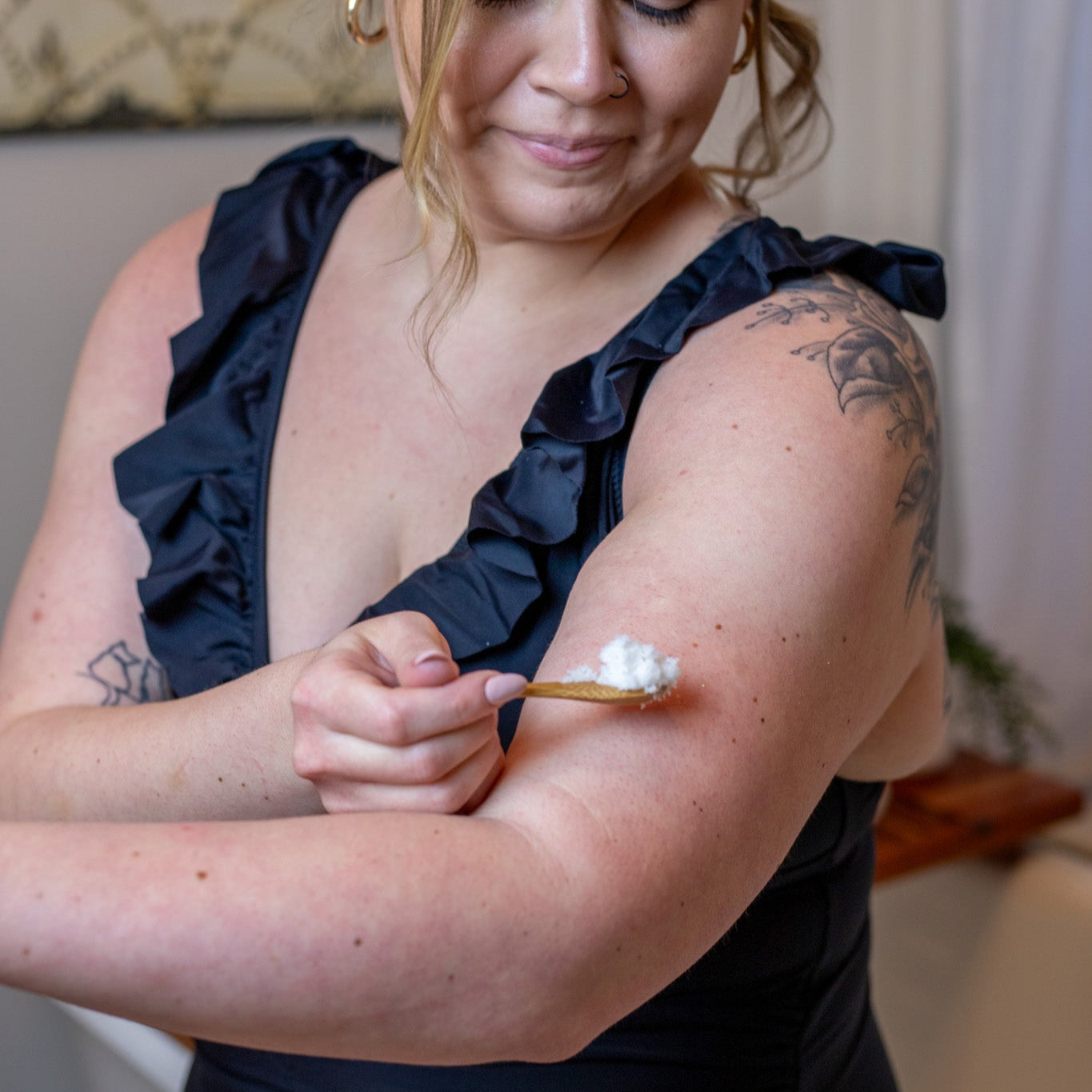 Woman applying exfoliating sugar scrub to arm with a bamboo spoon
