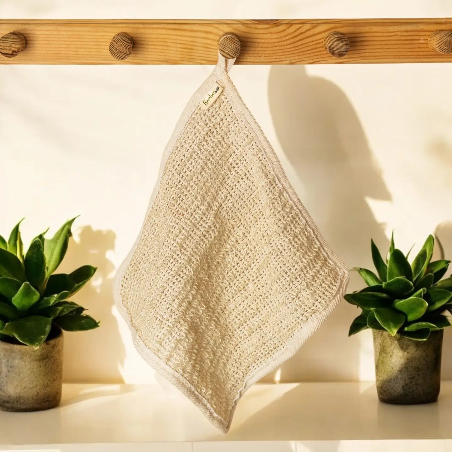Beige textured towel hanging on a wooden rack with two potted plants on either side.