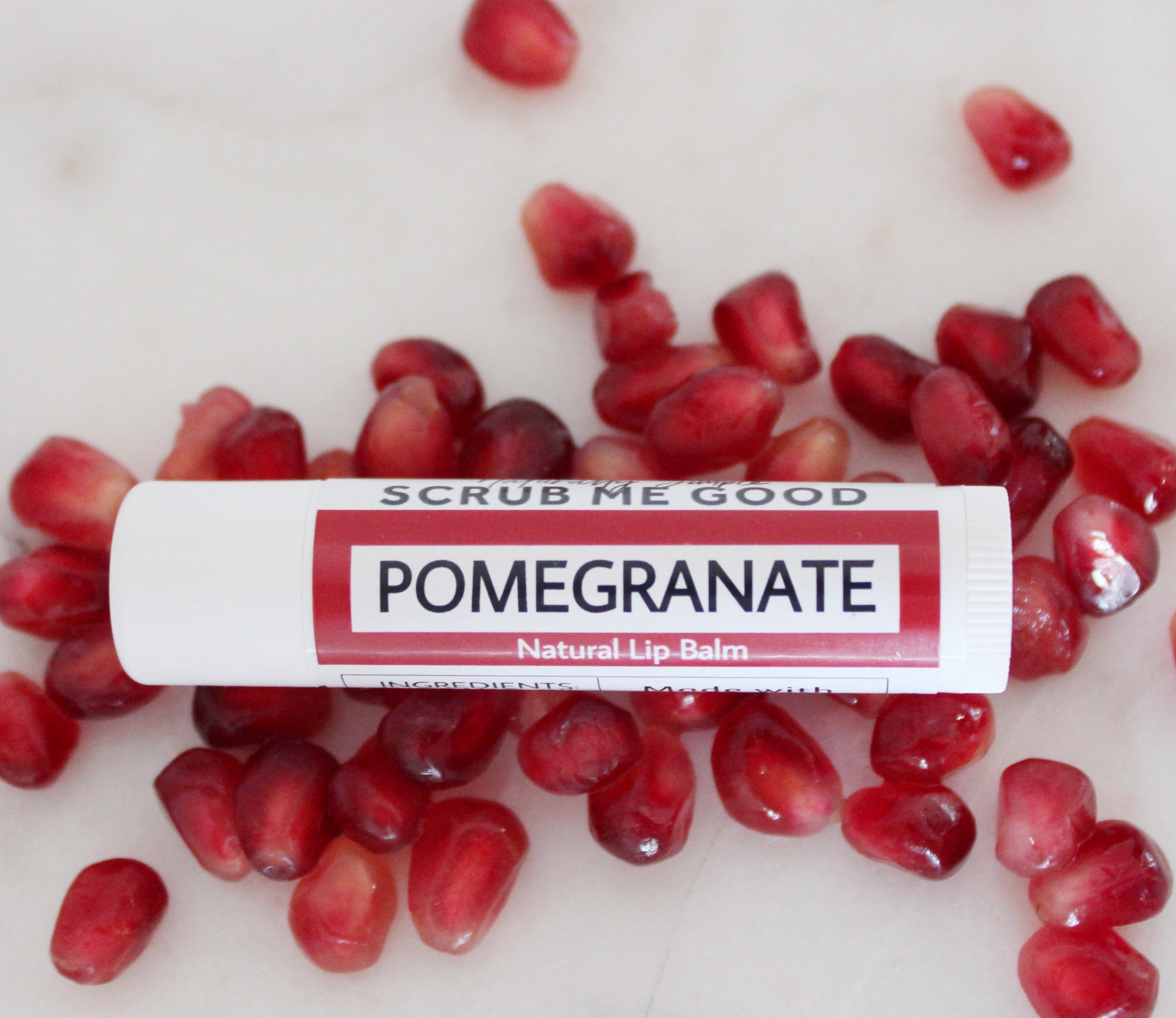 Pomegranate lip balm laying on a bed of pomegranate seeds