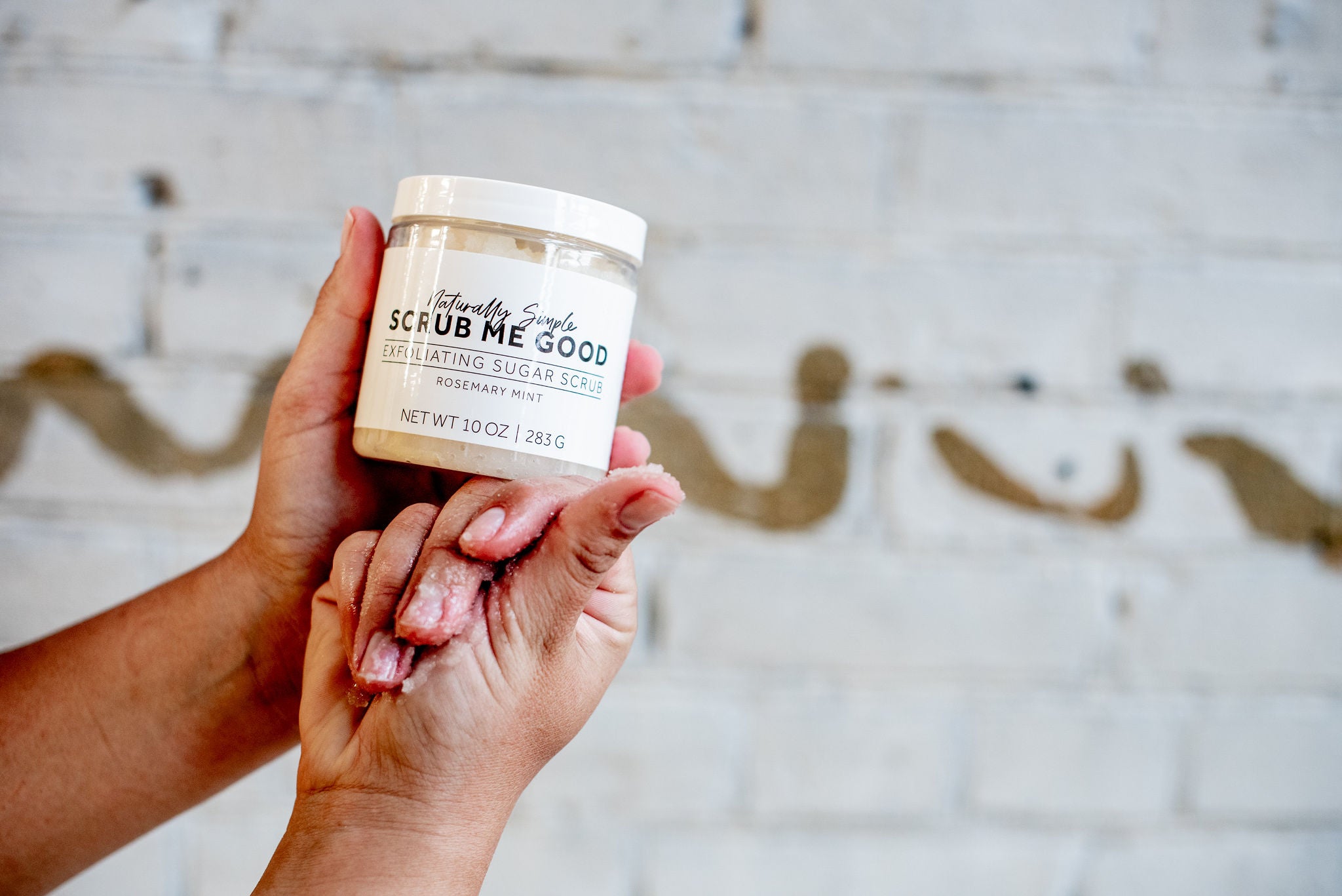 person holding rosemary mint sugar scrub with sugar scrub in their hand