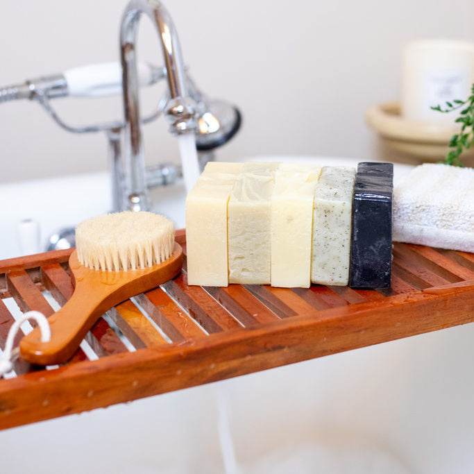 Bar soaps lined up on a wooden tray over a bathtub