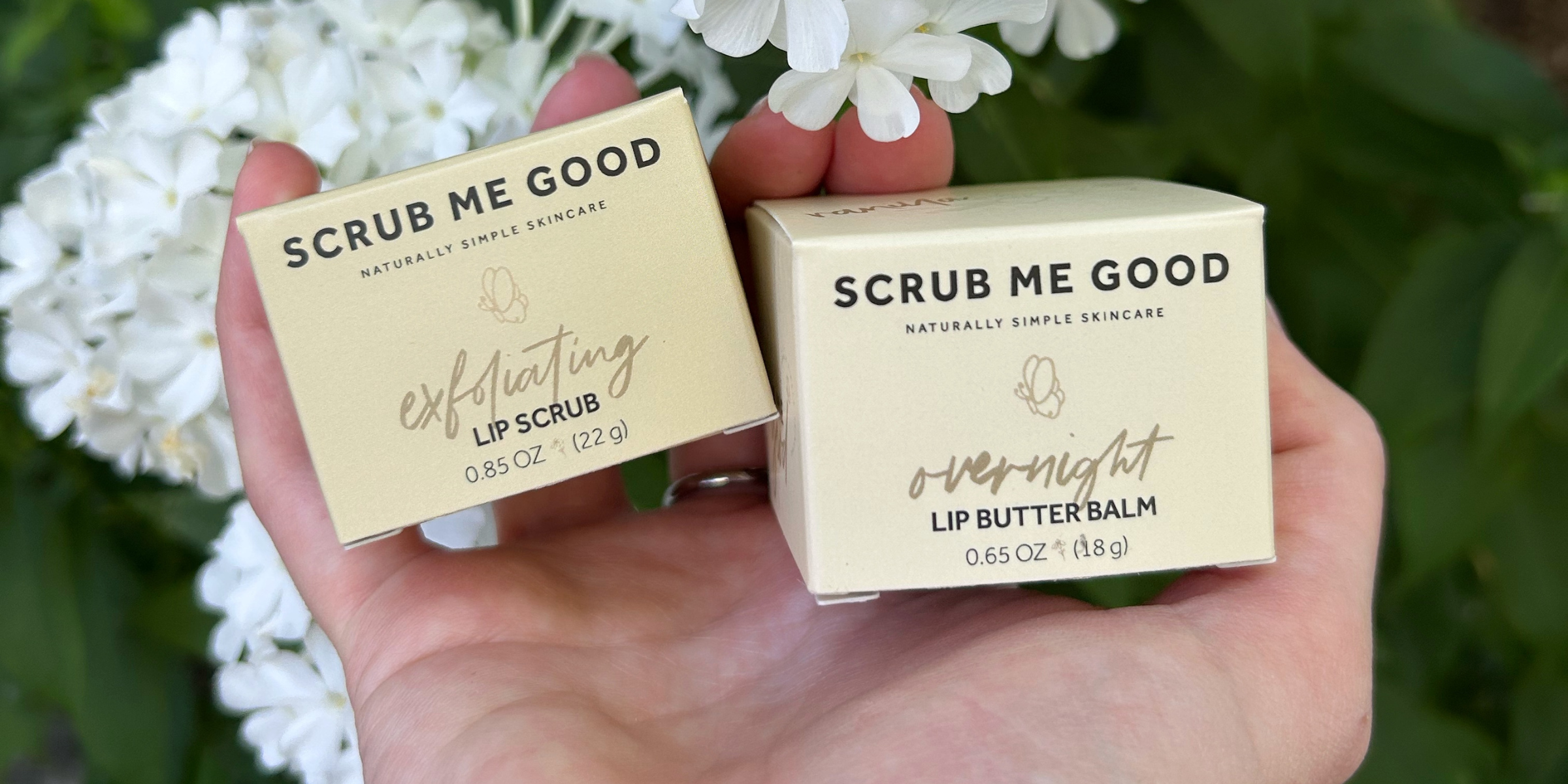 scrub me good lip scrub and lip butter balm being held in front of a floral background