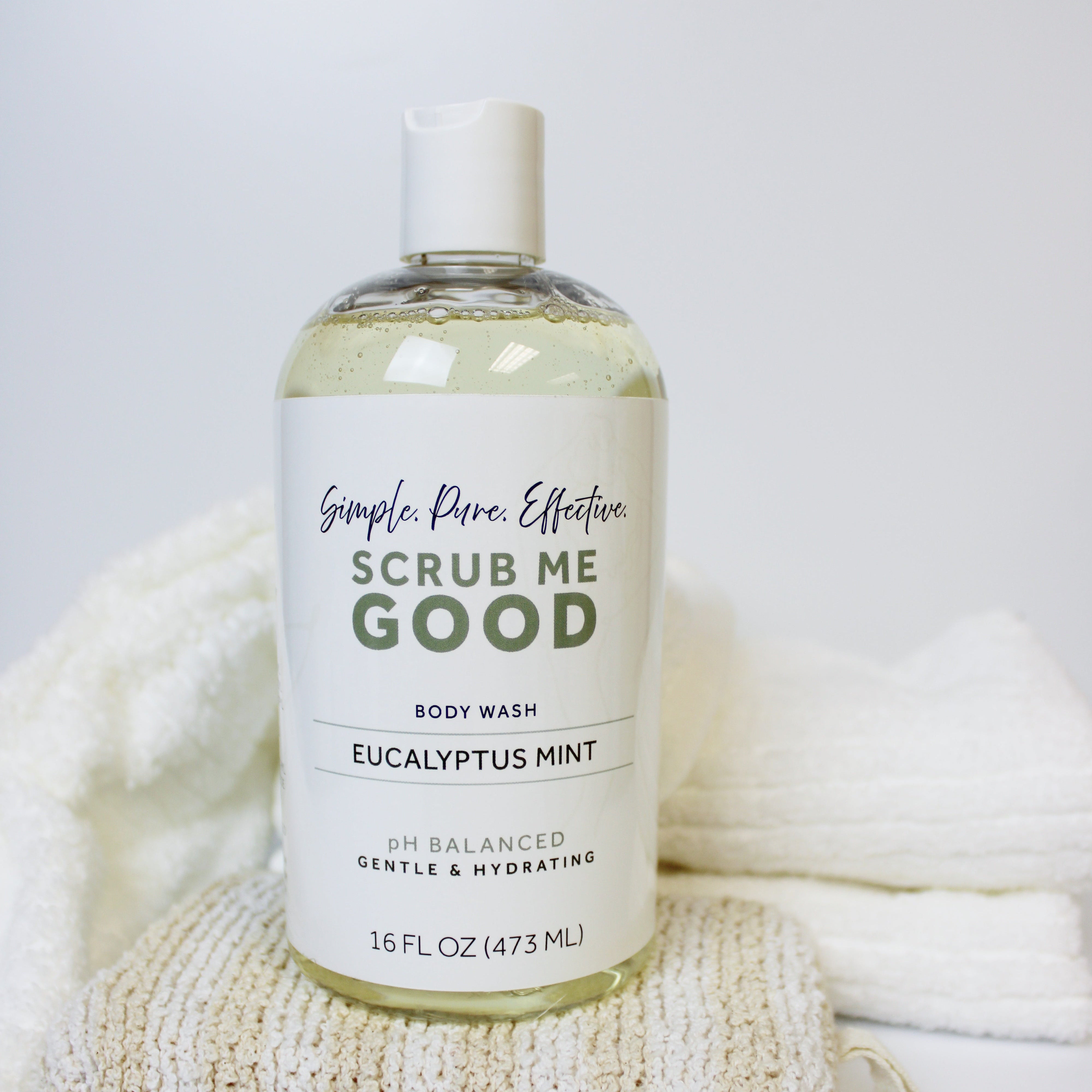 Bottle of Scrub Me Good body wash with a textured sponge on a white background