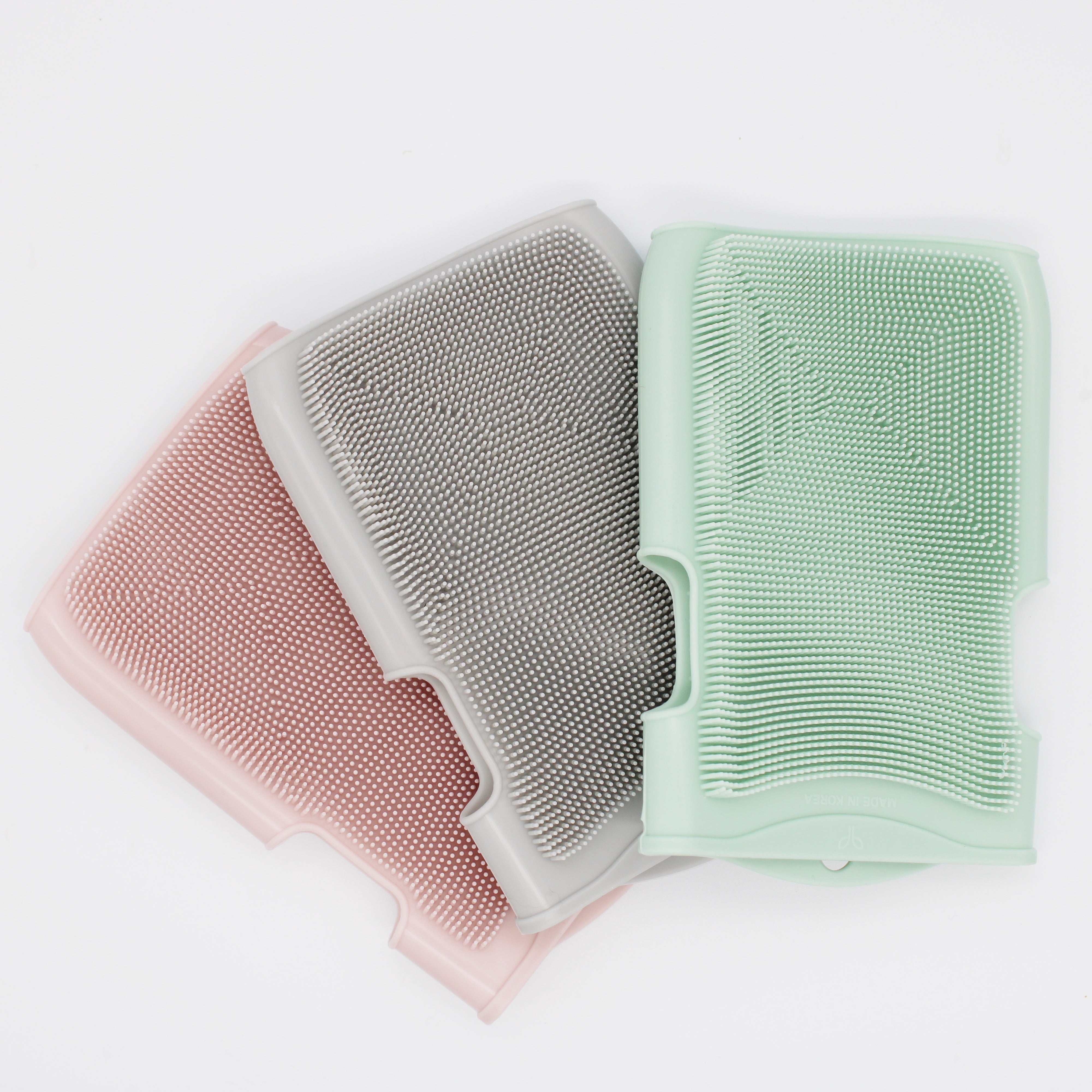 Three silicone sponges in pink, gray, and green on a white background