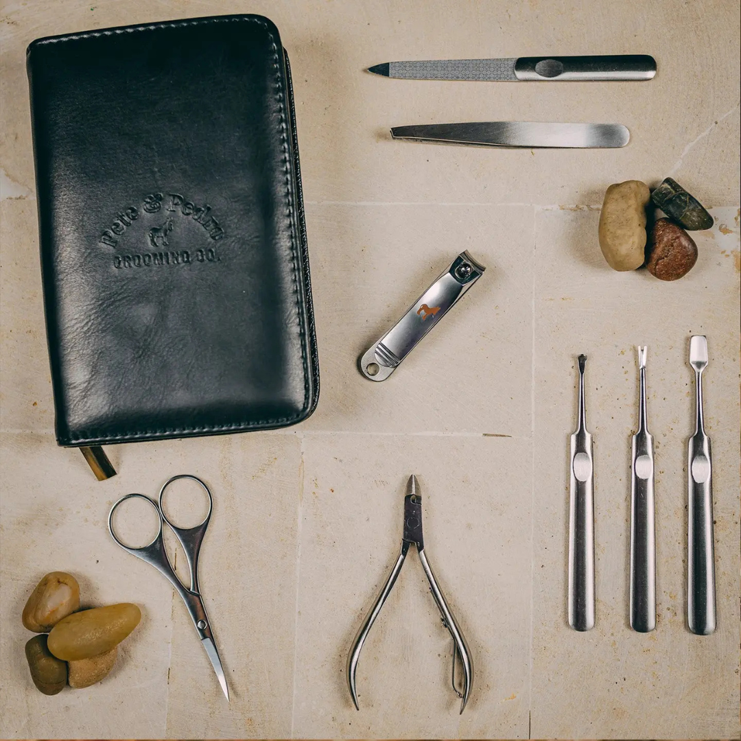 Open men’s manicure set showing stainless steel grooming tools secured inside a black leather zip case.